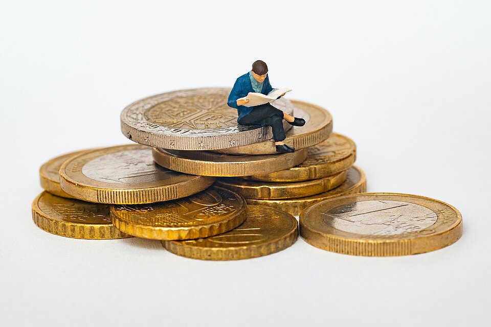 Grafik Mensch sitzt auf Euromünzen (Bild: Mathieu Stern/Unsplash)