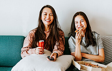 Zwei junge Frauen auf dem Sofa mit Pizza und Fernbedienung (Bild: rawpixel.com)