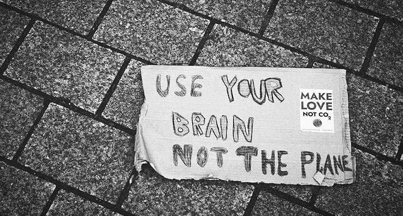 Plakat auf Pflaster „USE YOUR BRAIN NOT THE PLANET“ und „MAKE LOVE NOT CO2“ in N. Köbel: Umwelt und Bildung in mediendisurs 102 (Bild: © Christian Lue_unsplash)