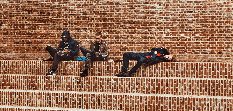 Jugendliche mit Smartphones auf einer Mauer (Bild: Maria Teneva/Unsplash)
