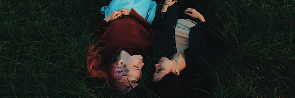 Zwei Frauen liegen im Gras, einander zugewandt. (Bild: Masha/Unsplash)